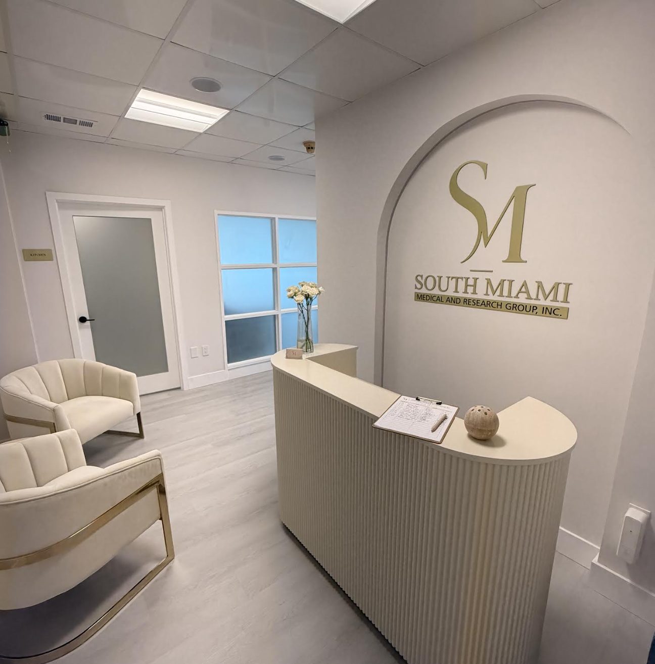 The clinic's reception, with the gold SM monogram on the wall above a fluted ivory desk